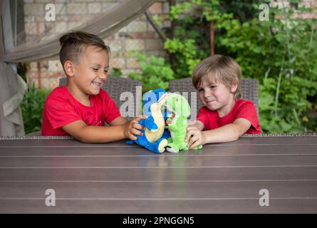 Zwei Jungs, die am Tisch sitzen, haben Spaß beim Rollenspiel mit Plüschdinosauriern. Stockfoto