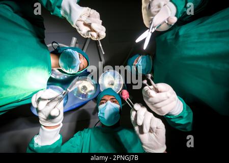 Chirurgen- und Krankenpflegegruppe in einem grünen Operationskittel, die chirurgische Operationen im Operationssaal durchführt. Ansicht von unten. Chirurgische Notfallversorgung conce Stockfoto