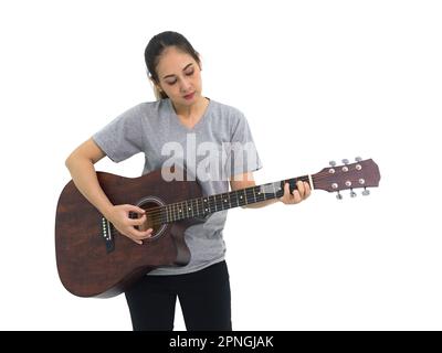 Asiatische Frau in grauem T-Shirt und schwarzer Hose, die akustische Gitarre spielt. Porträt auf weißem Hintergrund mit Studiolicht. Stockfoto