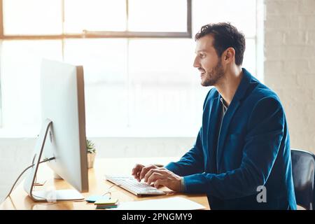 HES engagiert sich für den Erfolg. Ein attraktiver junger Geschäftsmann, der an seinem Computer in einem modernen Büro arbeitet. Stockfoto