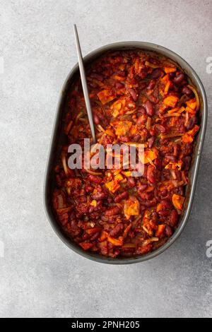 Gesundes Frühstück und Mittagessen, gedünstete rote Bohnen mit Karotten, Zwiebeln und Tomaten, Blick von oben auf eine ovale Keramikrösterei mit gedünsteten Hülsenfrüchten Stockfoto