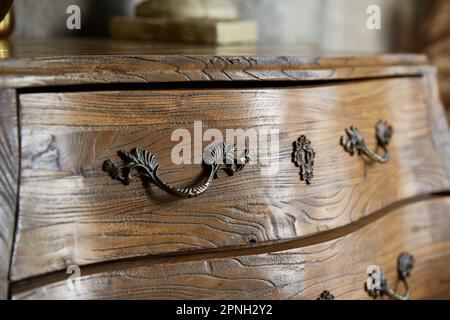 Vintage-Nahaufnahme mit gebogener Kommode. Geschmiedete Griffe. Stockfoto