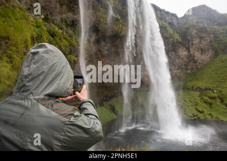 Seljalandsfoss, August 2021: Ein Tourist macht ein Foto von Seljalandsfoss, einem der berühmtesten Wasserfälle in Icealand, mit massivem Weißwasserstea Stockfoto