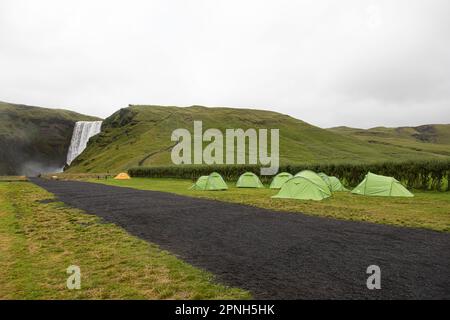 Skogafoss, Island - August 2021: Campingplatz mit Zelten mit dem im Hintergrund gelegenen Skogafoss Wasserfall, einem der berühmtesten in Island, Spritzen und Steami Stockfoto