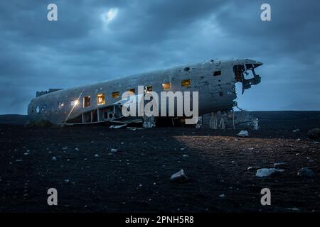 Island - August 2021: Lichteffekt in der Nacht des alten abgestürzten Flugzeugabsturzes, das an einem abgelegenen schwarzen Sandstrand in Island aufgegeben wurde Stockfoto