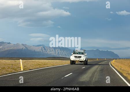 Island - August 2021: suv-Autos auf einer isländischen Straße mit wunderschöner grüner Landschaft und Bergen im Hintergrund Stockfoto