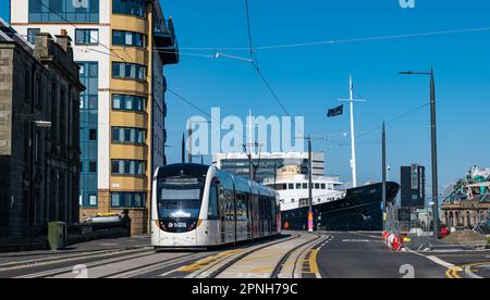 Leith, Edinburgh, Schottland, Großbritannien, 19. April 2023. Straßenbahnen nach Newhaven: Die ersten Straßenbahnen, die tagsüber auf der verlängerten Straßenbahnlinie verkehren, begannen heute, die Strecke zu testen. Abbildung: Eine Straßenbahn fährt am "Fingal Edinburgh" vorbei, einem luxuriösen schwimmenden Hotel. Kredit: Sally Anderson/Alamy Live News Stockfoto