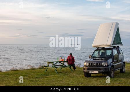 Vestmannaeyjar, Island - August 2021: Ein Auto mit einem Zelt auf dem Dach mit Touristen auf einem Campingplatz in der Nähe von Husavik, mit wunderschöner grüner Landschaft und oc Stockfoto