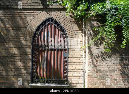 Geschlossenes Fenster mit Fensterläden in der alten Backsteinmauer. Schatten und Efeu-Blätter an der Ziegelwand. Natürlicher Hintergrund im Freien Stockfoto