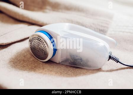 Nahaufnahme des kabelgebundenen Fusselentferners. Reinigung der Kleidung mit einem elektrischen Fuzz-Rasierer zu Hause. Rasieren der Pille vom Mantel mit einer modernen Maschine Stockfoto