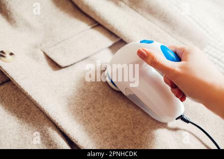 Frau, die zu Hause mit einem Fuzz-Rasierer Fusseln von der Kleidung entfernt. Nahaufnahme des kabelgebundenen elektrischen Handgeräts. Ich kümmere mich um die Kleidung. Haushaltsmaschine Stockfoto