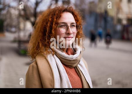 Das natürliche Porträt einer pensiven weissen Ingwerfrau mit Sommersprossen und Lockenhaaren. Stockfoto