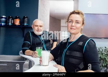 Lächelnde Männer und Frauen in der notaufnahme sind Anzüge für Getränkehändler in der Sportbar. Ältere Ehepaare kommunizieren und erholen sich vom Training mit elektrischen Muskelreizen Stockfoto