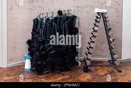 Schwarze ems-Trainingswesten im Fitnessclub. Elektrische Muskelstimulation. Spezielle Sportuniform vor dem Hintergrund von Ständer mit Kurzhanteln. Frei sp Stockfoto