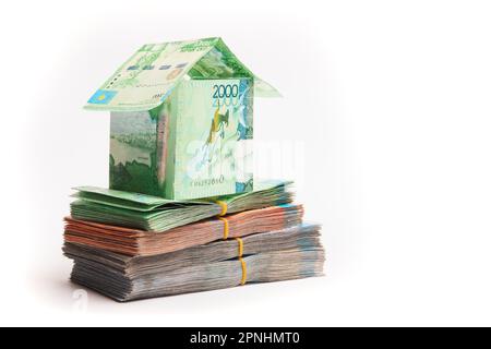 Ein Haus aus kasachischem Geld, das aus Banknoten gemacht ist, steht auf Päckchen voller Tänge. Hypothekenkonzept, Immobilienaufwertung, Kopierraum Stockfoto