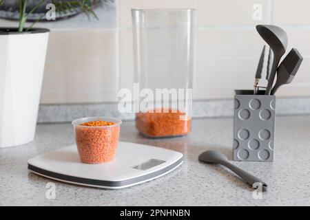 Gesundes Essen oder Diät-Konzept. Küchenwaage mit Messbecher und Linsen auf dem Küchentisch Stockfoto