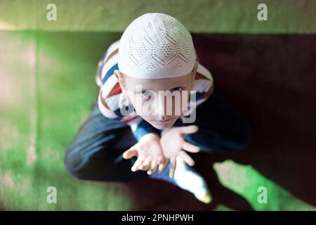 Blick von oben auf den jungen muslimischen Jungen, der während des heiligen Monats Ramadan betet, in der modernen Moschee Stockfoto