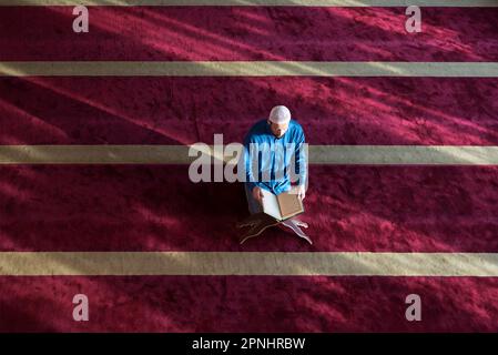 Arabischer muslimischer Mann, der traditionelles Gebet für Gott macht und Koran liest, während er während des ramadan traditionelle arabische Kleidung trägt Stockfoto