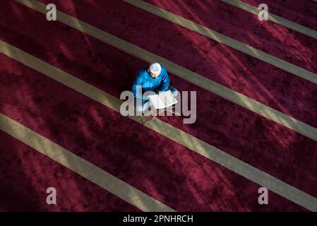Arabischer muslimischer Mann, der traditionelles Gebet für Gott macht und Koran liest, während er während des ramadan traditionelle arabische Kleidung trägt Stockfoto