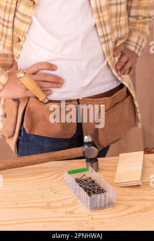 Hoher Winkel des Ernteguts, anonymer Zimmermann, der mit Instrumenten neben einer Werkbank steht Stockfoto