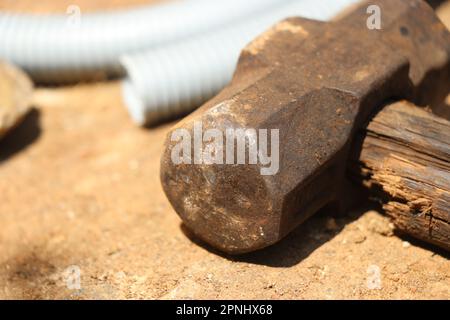 Alter und rostiger Hammer mit gebrochenem Holzgriff, der auf einer Außenleuchte auf dem Boden gehalten wird Stockfoto