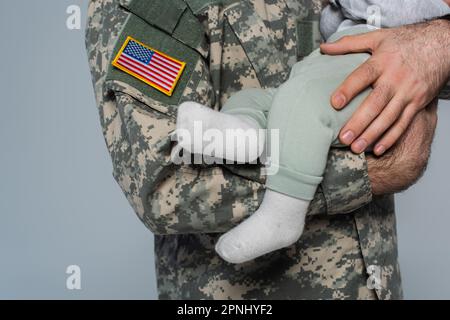 Schnittbild eines US-Soldaten in Uniform, der den neugeborenen Sohn auf grau isoliert hält Stockfoto