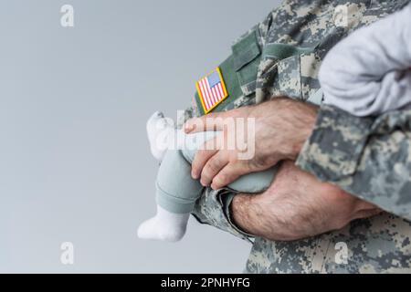 Schnittbild eines amerikanischen Soldaten in Uniform, der ein Neugeborenes isoliert auf grau hält Stockfoto