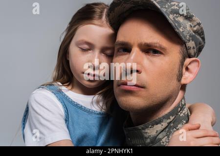 Trauriges Mädchen umarmte Vater in Militäruniform und weinte während des Gedenkfeiertags isoliert auf Grau Stockfoto