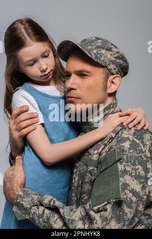 Trauriges Mädchen umarmte einen Soldaten in Militäruniform, weinend während des Gedenkfeiertags, isoliert auf Grau Stockfoto