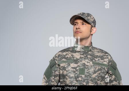 Amerikanischer Patriot in Militäruniform mit Mütze, der während des Gedenkfeiertags wegblickt, isoliert auf Grau Stockfoto