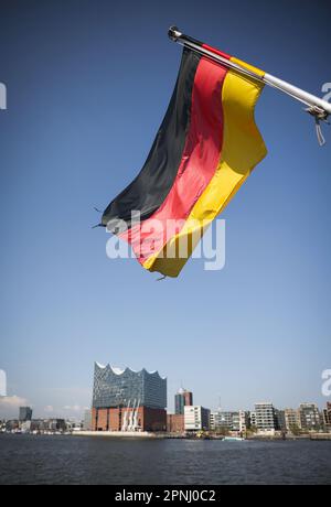 Hamburg, Deutschland. 17. April 2023. Eine deutsche Flagge fliegt am Heck eines Ausflugsschiffs im Hamburger Hafen über der Elbphilharmonie. Kredit: Christian Charisius/dpa/Alamy Live News Stockfoto