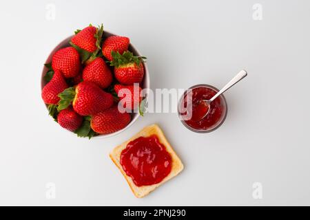 Ein Blick von oben auf das mit Erdbeermarmelade gefüllte Brot und Erdbeerfrüchte auf weißem Hintergrund Stockfoto