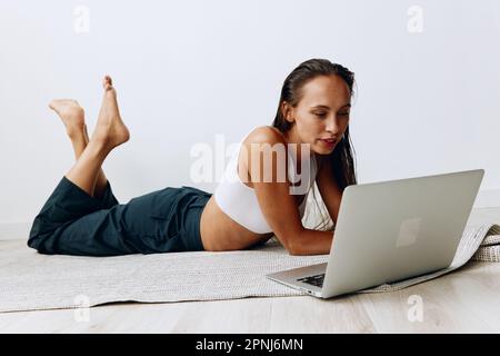 Eine Frau geht auf dem Boden Sport treiben, mit einem Online-Trainer über einen Laptop. Sport in Abriegelung Stockfoto