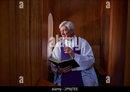 Der Oberpriester liest Gebete aus der Bibel, während er mit dem Sünder spricht, während er in der Beichte beichtet Stockfoto