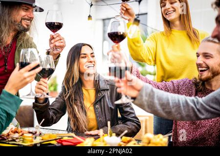 Trendige Leute, die Spaß beim Toasten von Rotwein im heimischen Weingarten haben - glückliche Freunde, die sich im Open-Air-Restaurant Diner treffen Stockfoto