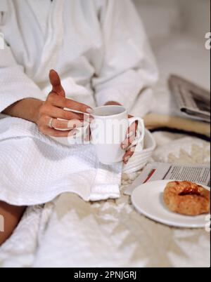 Eine Frau im weißen Bademantel frühstückt im Bett Stockfoto