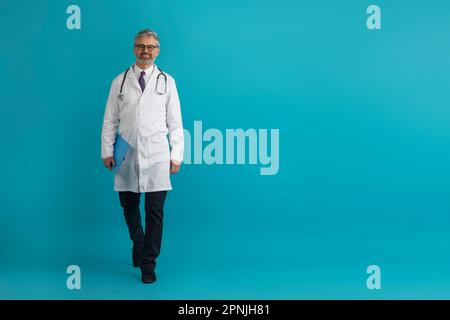 Fröhlicher Arzt mittleren Alters mit Krankenblatt auf blau Stockfoto