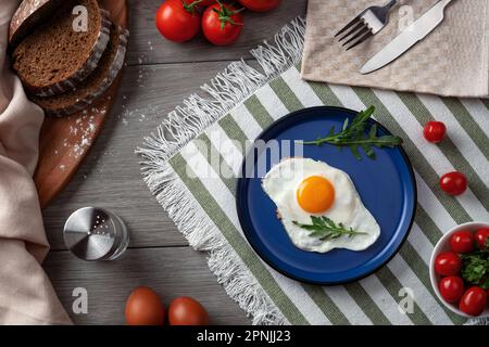 Spiegeleier zum Frühstück. Gesundes Frühstück mit Gemüse und Kräutern. Spiegelei auf einem blauen Teller. Auf dem Tisch servieren Stockfoto