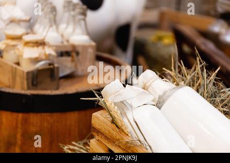 Glasflaschen mit frischer natürlicher Milch, Aluminiumdosen auf Heu auf Milchviehbetrieben. Gesunde landwirtschaftliche Erzeugnisse Stockfoto