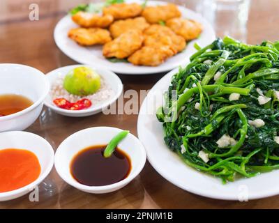 Vietnamesische gebratene Morgenpracht, rau muong xao toi und vietnamesische Fischkuchen, cha Ca quy nhon, unscharf im Hintergrund. Gebratener Morgengloria schon Stockfoto