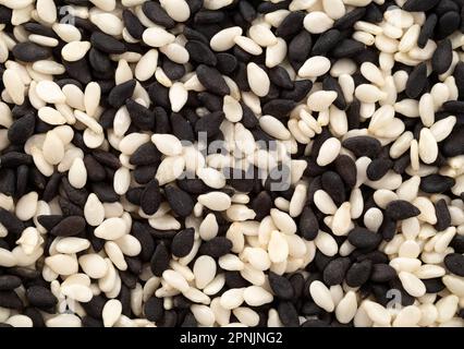 Stapel schwarzer und weißer Sesamsamen als Hintergrund, Draufsicht. Makro. Extreme Nahaufnahme. Stockfoto