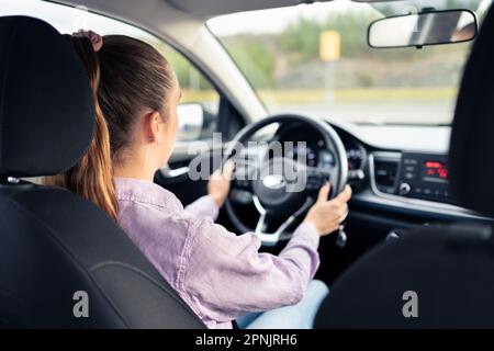 Frau, die Auto fährt. Junger Fahrer. Fahrzeugtest im Händlerbetrieb oder Schülerschulung in der Schule, um eine Lizenz zu erhalten. Hände am Lenkrad. Stockfoto