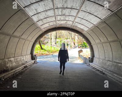 Frau geht durch einen Brückentunnel im Prospect Park in Brooklyn, New York. Stockfoto