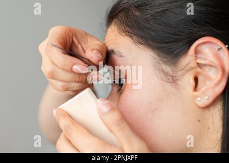 Nahaufnahme einer Frau mit Pinzette, die ihre falschen Wimpern mit großer Sorgfalt anlegt Stockfoto