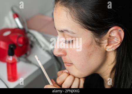 Junge Latina-Frau, die ihr Kinn in einem kleinen Spiegel ansieht und ihre Lippen zusammendrückt, um einen besseren Blick zu bekommen. Stockfoto