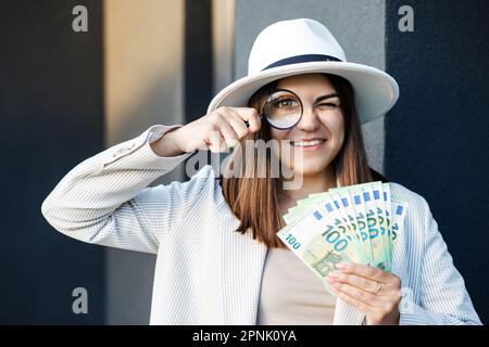 Attraktive Frau mit Bargeld in den Händen und Lupe. Stockfoto