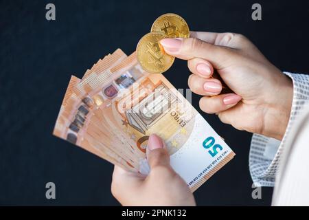 Nahaufnahme die Hände der Frauen halten Goldmünzen der Krypto-Währung und Euro-Banknoten in weißer Jacke. Stockfoto