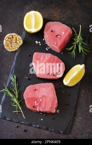 Meeresfrüchte. Rohe saftige Thunfischsteaks mit Gewürzen und Rosmarin auf einem Steintisch. Stockfoto