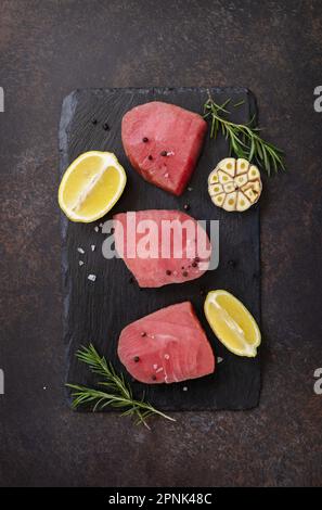 Meeresfrüchte. Rohe saftige Thunfischsteaks mit Gewürzen und Rosmarin auf einem Steintisch. Blick von oben. Stockfoto