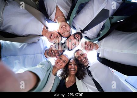 Selfie einer Gruppe von Geschäftsleuten, die sich im Kreis umarmten, mit dem Gesicht nach unten lächelten und in die Kamera schauten. Stockfoto